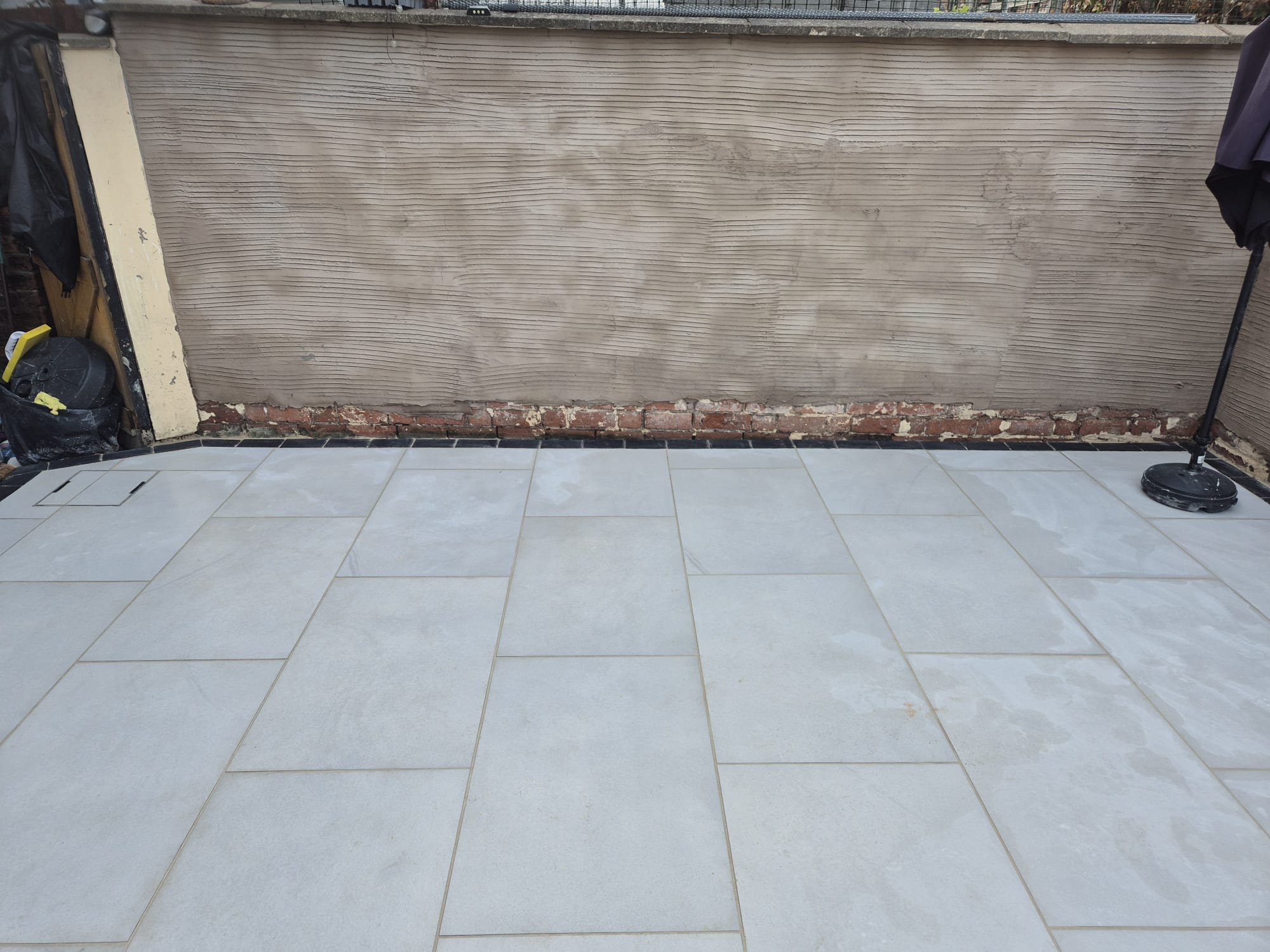 Smooth grey porcelain patio laid against a rendered garden wall