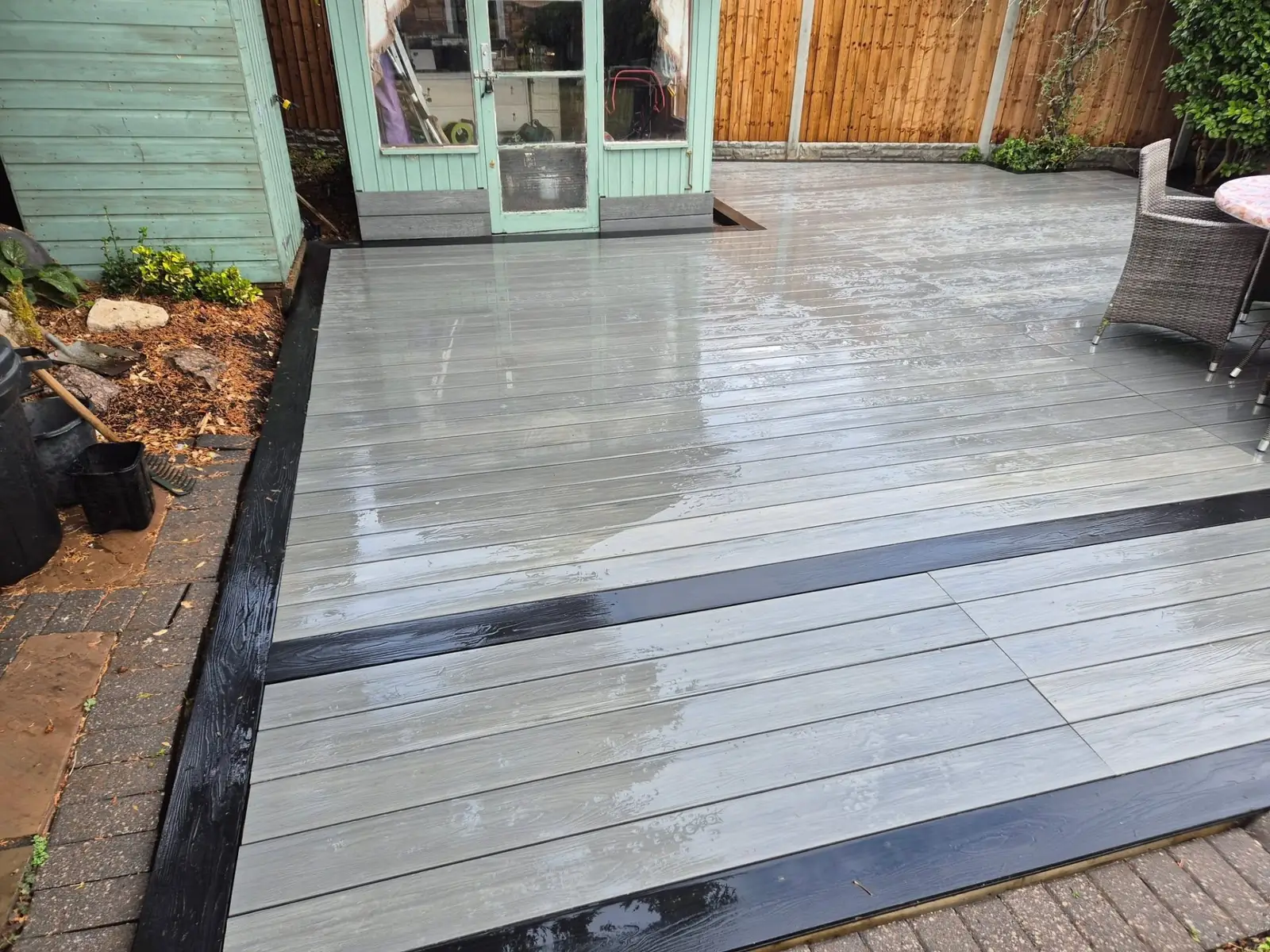 Light grey composite decking with a dark anthracite picture-frame border, laid across a Wirral back garden