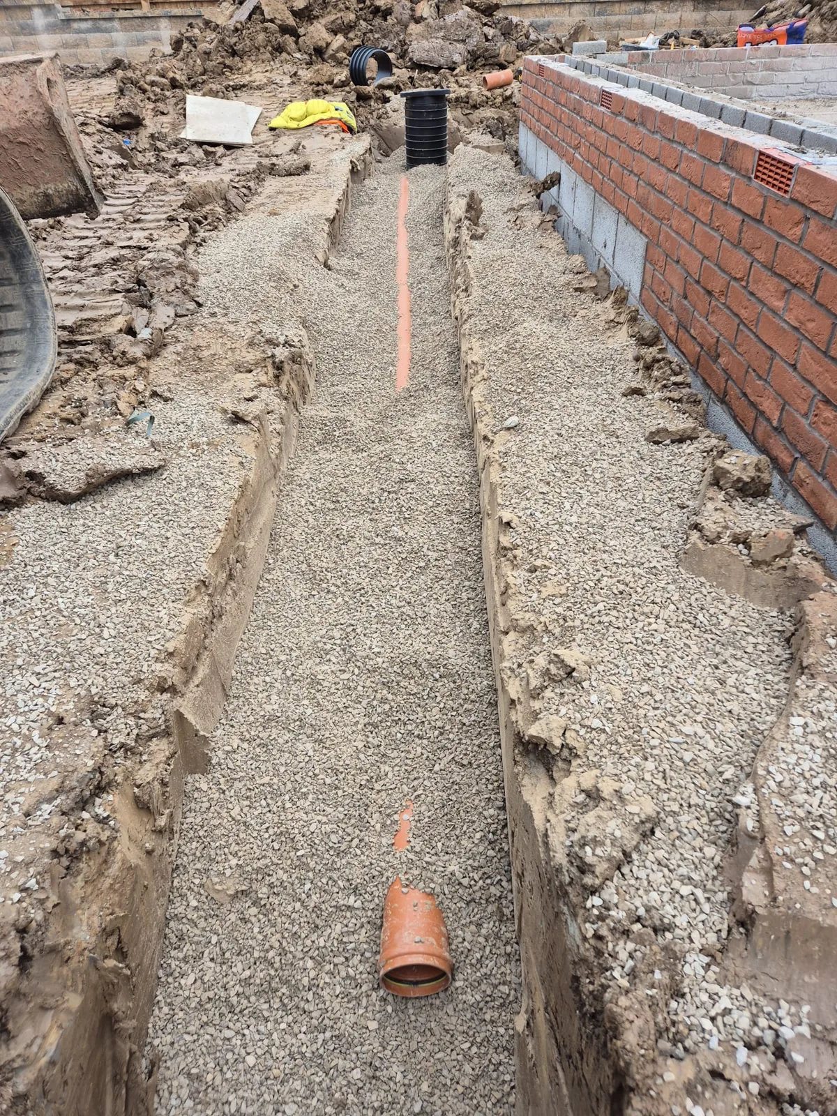 A drainage pipe bedded in gravel along a trench next to a new brick wall