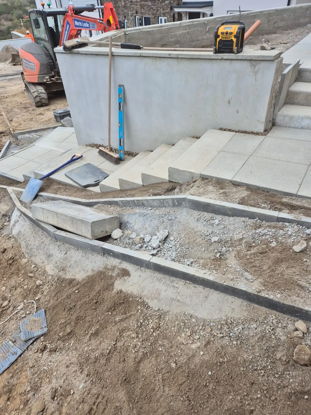 A concrete retaining wall with steps and paving, built to level with a mini digger on site