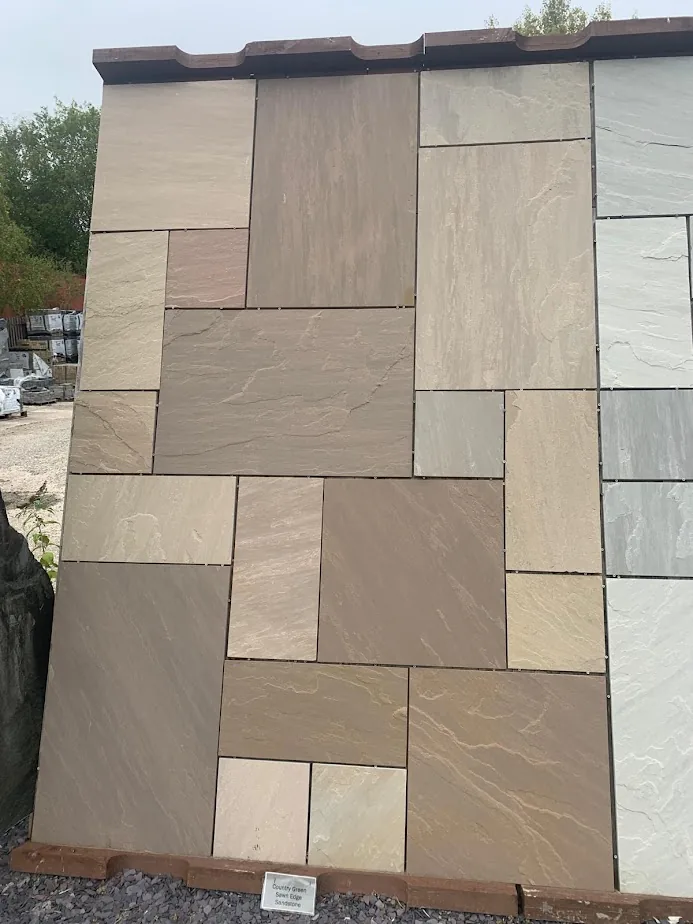 Country Green Sandstone sawn-edge paving display board at CED Wirral Depot in Hooton — warm greenish-browns and buffs with hints of pink and grey, naturally riven, shown in a mix of four sizes