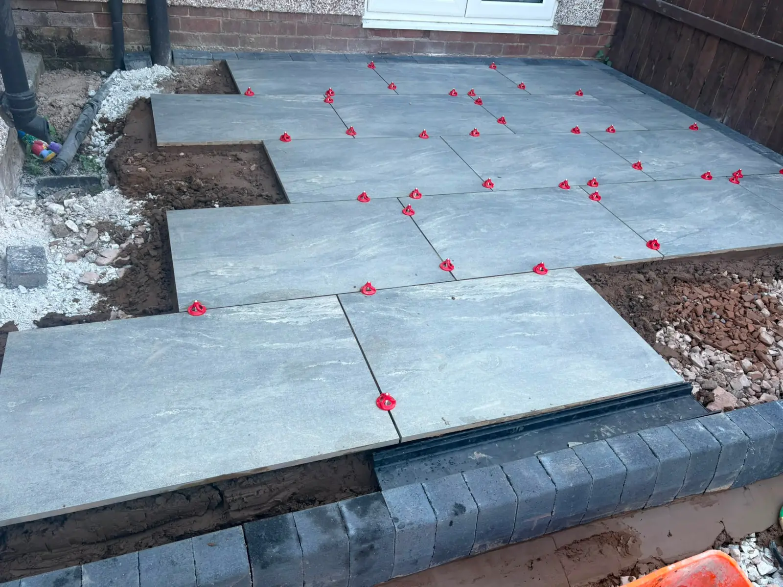 Raised porcelain patio mid-lay with tile spacers and drainage channel