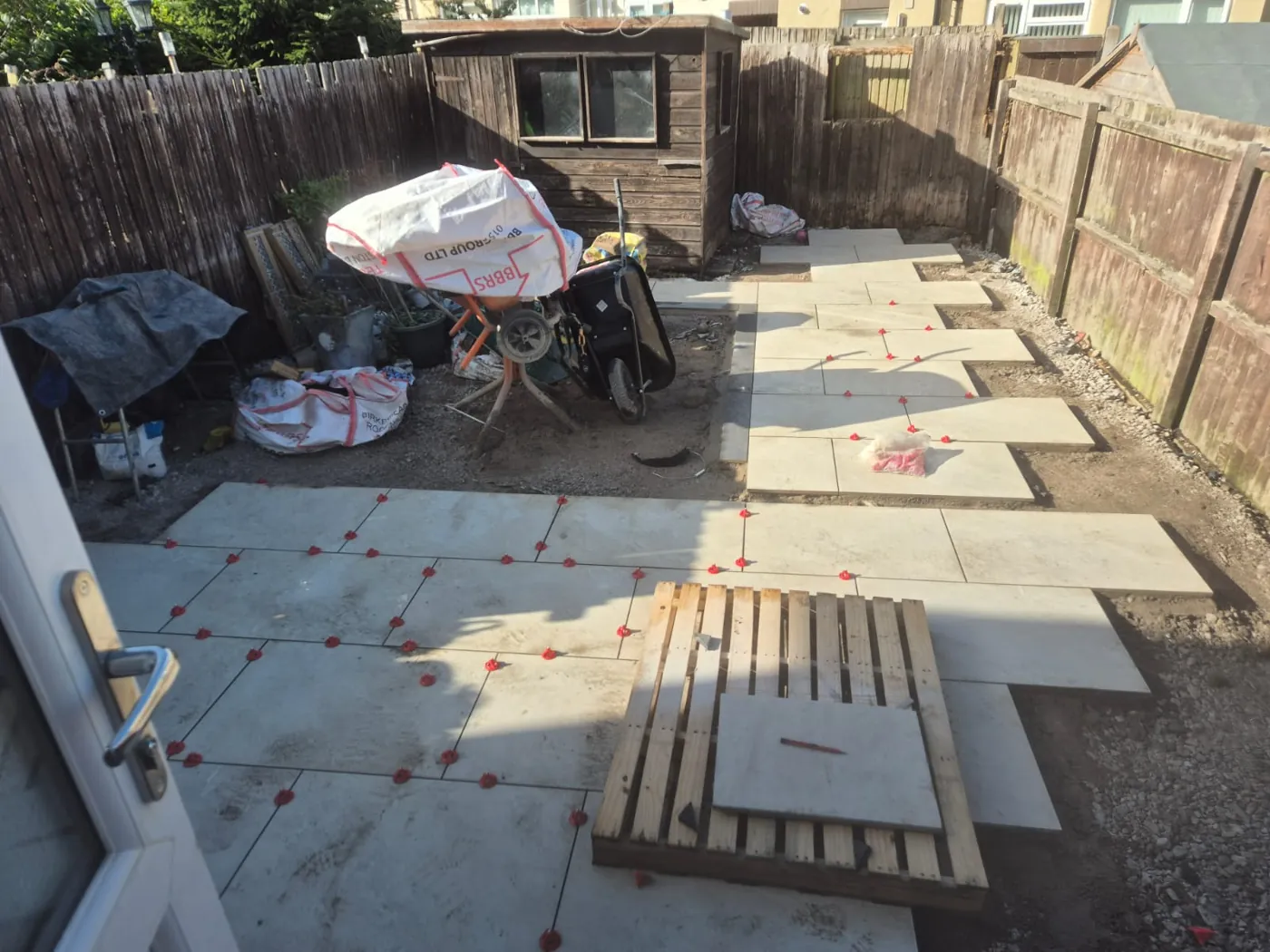 Light porcelain paving laid across most of a Birkenhead rear garden, running from the back door around the shed to the rear boundary, with charcoal block edging and levelling clips still in place