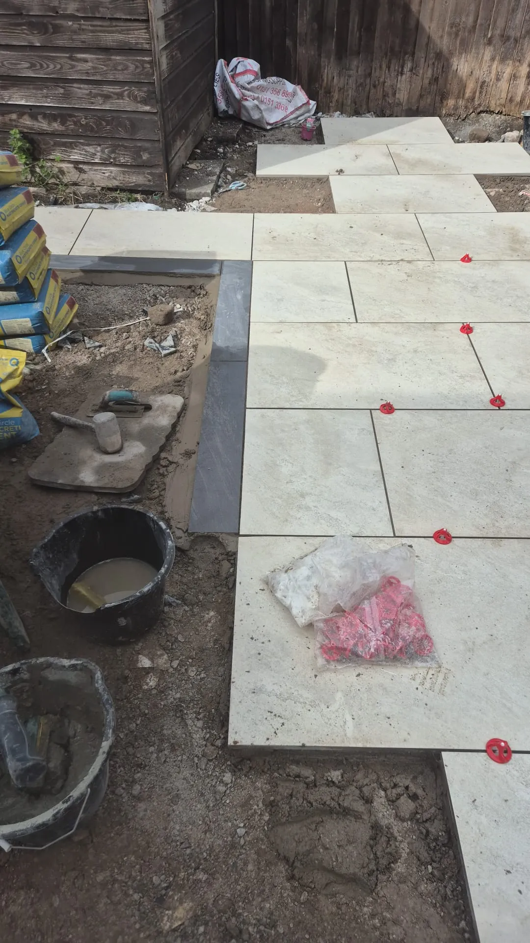 Light porcelain slabs laid on a full mortar bed in Birkenhead, levelling clips still in place, with the charcoal block edging running alongside
