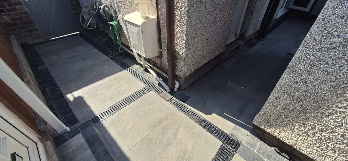 Raised charcoal porcelain patio with a linear drainage channel and a band of dark setts