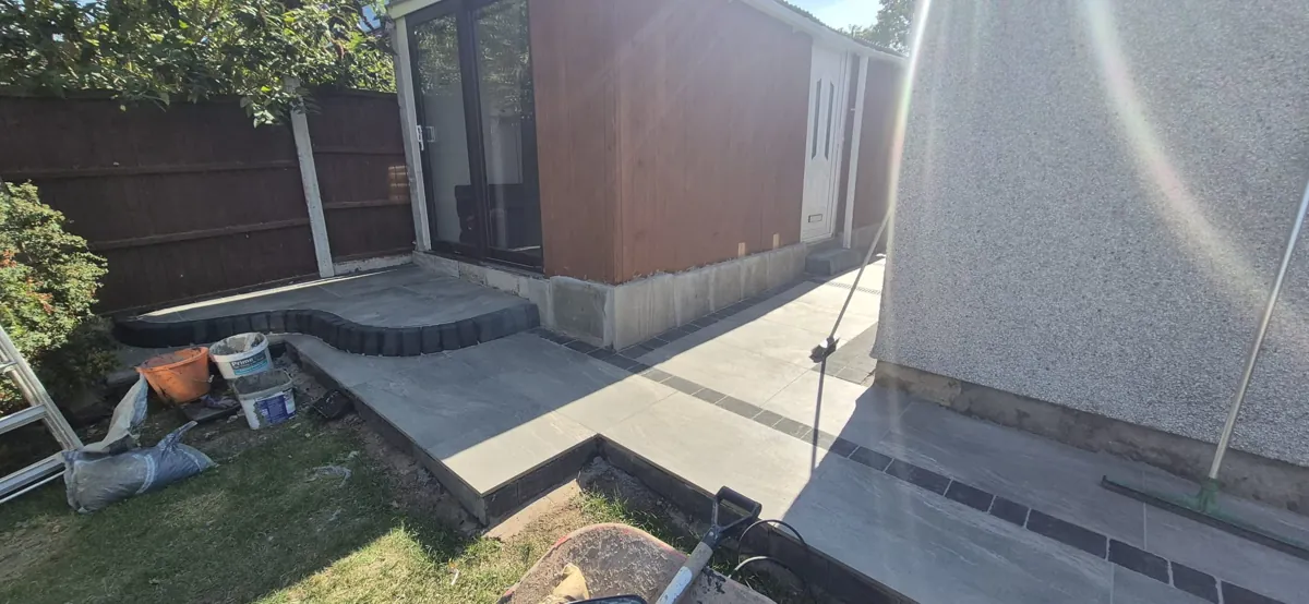 Charcoal porcelain path with a dark setts border sweeping round to a timber-clad garden room